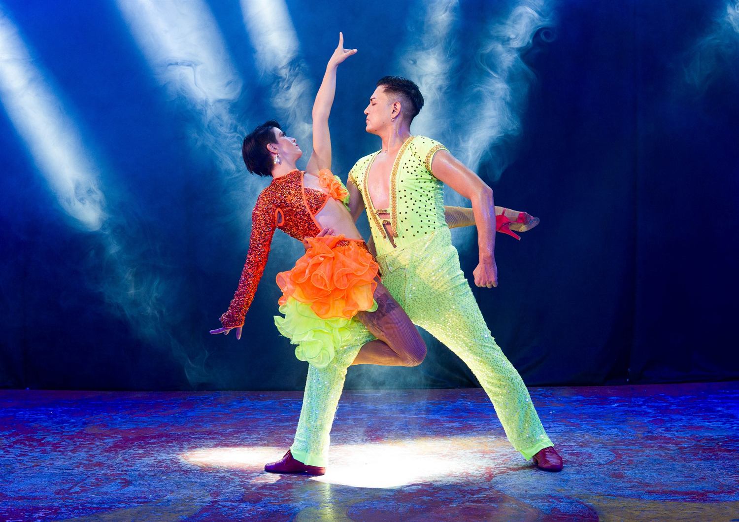 A couple in neon lime and orange held mid-turn in blue light