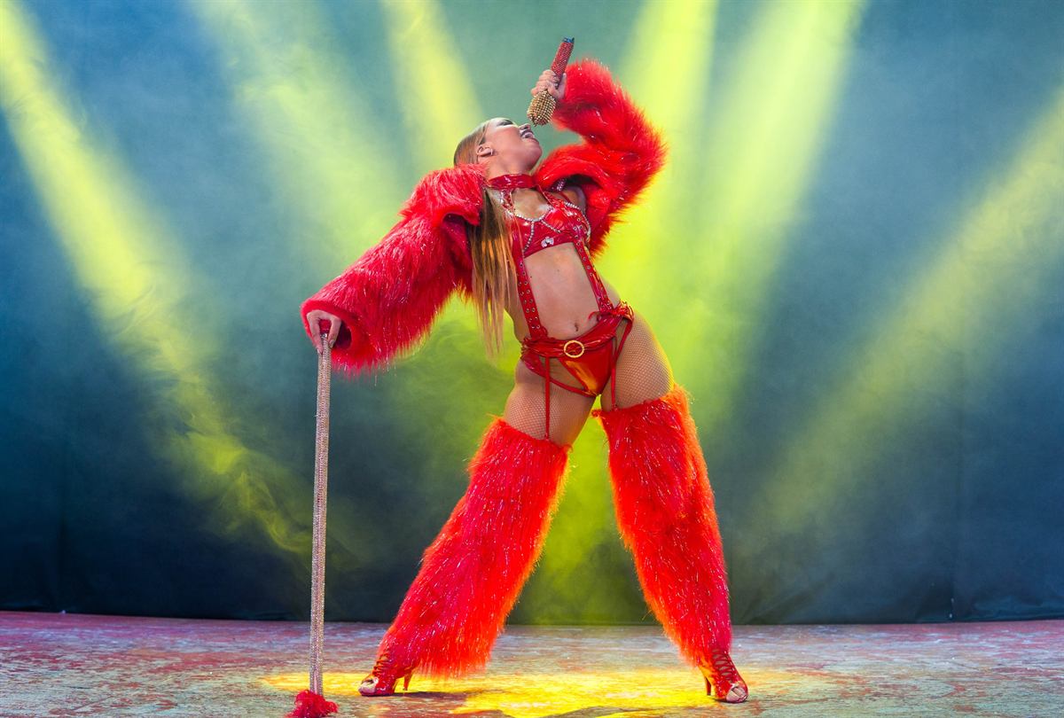 The singer standing in red fur under green beams
